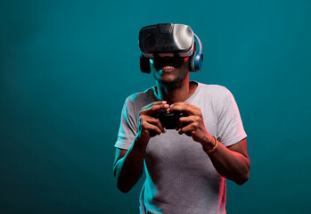 African american guy playing video game with controller and vr headset, enjoying online play with futuristic 3d simulation in studio. Gamer with virtual reality glasses holding joystick. © DC Studio