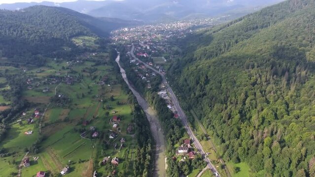 Stunning aerial shot of a small town near a river, in the mountains in summer, on a bright sunny day