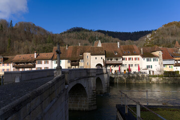 Fototapeta na wymiar Chalk stone bridge over the river Doubs at little medieval town St-Ursanne, Canton Jura, on a sunny winter morning. Photo taken February 7th, 2022, Saint-Ursanne, Switzerland.