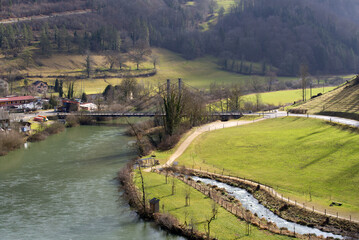 Aerial view of rope bridge near small medieval town Saint-Ursanne with river Doubs and defocus trees in the foreground on a winter day. Photo taken February 7th, 2022, Saint-Ursanne, Switzerland.