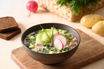 Homemade summer Okroshka soup with kefir and summer vegetables on light wooden table. Close up.