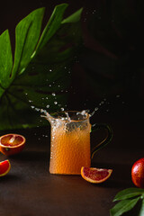 Orange juice splash. Fresh orange juice in a glass decanter and red orange fruit slices on on a dark background.