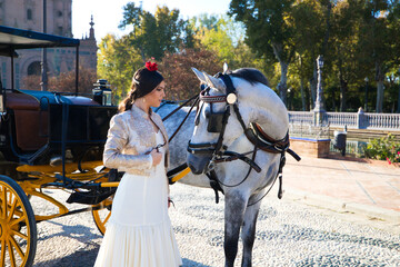 Flamenco dancer woman, brunette and beautiful typical spanish dancer is caressing a white horse in a square in seville. Flamenco concept of cultural heritage of humanity.