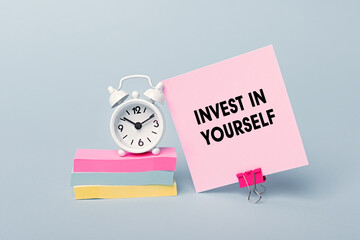 Invest In Yourself - concept of text on pink sticky note. Closeup of a personal agenda. Alarm clock and colorful stickers light blue background