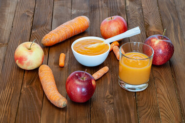 Carrot and apple puree in a glass jar and porcelain bowl on a natural wood table.
