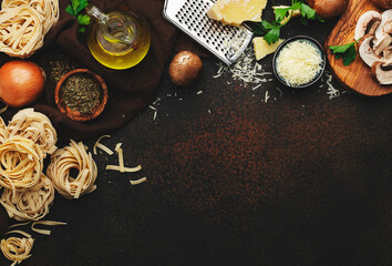 Italian uncooked pasta, brown champignons mushrooms, vegetables, cheese and ingredients for tasty cooking on old kitchen table background, dark style, top view. Food banner
