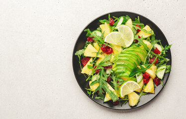 Vegan vegetarian salad with pineapple, arugula, avocado and dried cherry on white stone kitchen table, top view. Healthy eating, clean diet food, weight loss concept