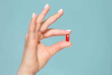 Close-up of a hand with one red pill, on a blue background. Copy paste. The concept of saving drugs.