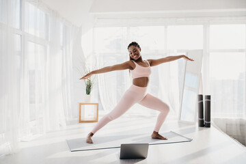 Fototapeta na wymiar Joyful fit young black woman practicing yoga at home, standing in warrior pose, copy space