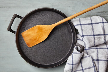 Empty round cast iron pan, wooden spatula, and tea towel napkin