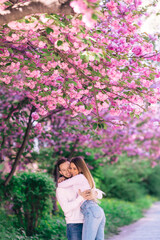 Emotional young couple. Man twists a woman in the spring park. Sakura tree blooming.