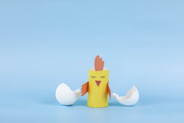 paper craft in the form of a yellow chicken hatched from an egg on a blue background, the concept...