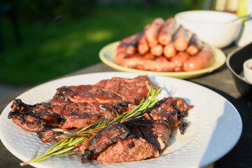 Meat steak and sausages grilled on barbecue served with rosemary. BBQ. Festive summer barbecue party. Outdoors. Close up.