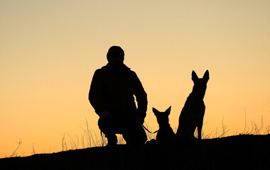 Fototapeta na wymiar Silhouettes of a man and two dogs on a sunset background, Belgian shepherd malinois dogs together