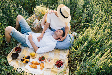 Romantic couple resting in a wheat field top view. Summer vacation relaxation freedom, picnic in nature. The concept of organic farming and healthy lifestyle, healthy food, happiness and joy