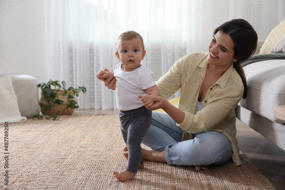 Wall mural Mother supporting her baby daughter while she learning to walk at home