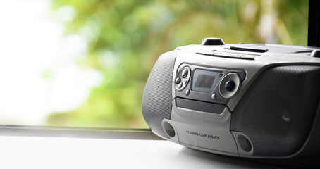 Cassette and CD player in 1990 style on window with natural blurred background. 1990’s vintage...