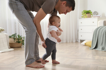 Father supporting his baby daughter while she learning to walk at home