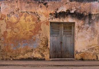 Old grunge cracked concrete wall with some stains and holes. White brown and orange collors. with old door
