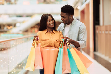 Happy black couple holding shopping bags looking at each other - obrazy, fototapety, plakaty
