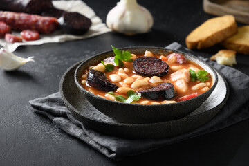 Fabada with chorizo, morcilla, sausage, haricot on black background. Spanish traditional warming dinner. Close up.