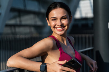 Fototapeta na wymiar Smiling joyful woman with smartphone posing for camera outdoors