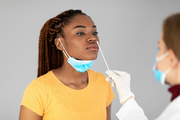 Millennial black woman making nasal covid-19 swab test on grey studio background. Viral disease...