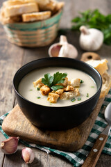 Garlic soup topped with croutons in bowl on wooden table
