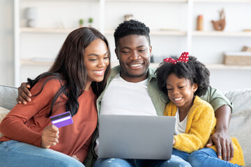 Online Purchases. Black Family With Little Daughter Using Laptop And Credit Card
