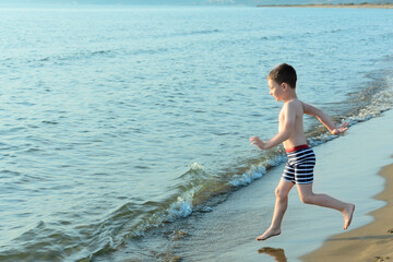Happy child boy joyfully runs to swim in the sea. Summer and travel concept