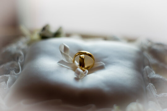 Romantic image of two gold wedding rings on white cushion with blurred background.