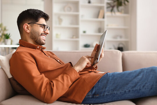 Smiling Young Arab Man Using Digital Tablet At Home