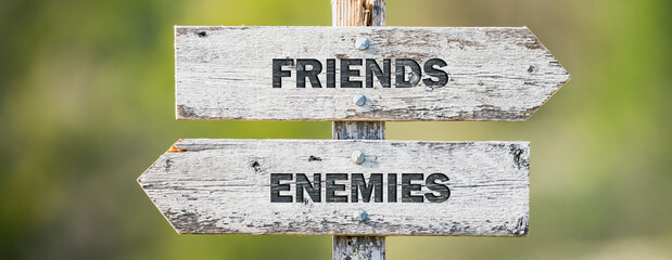 opposite signs on wooden signpost with the text quote friends enemies engraved. Web banner format.