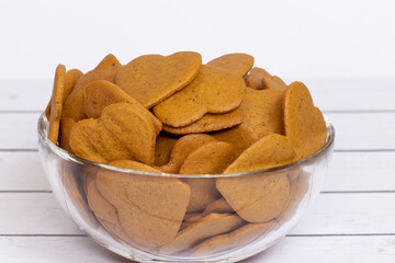 Heart-shaped cookies in a glass bowl on a wooden, light background. Close-up. Selective focus.