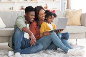 Happy african american family of three relaxing with laptop at home