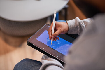 A close up shot of a man's hands using a stylus to draw on a tablet