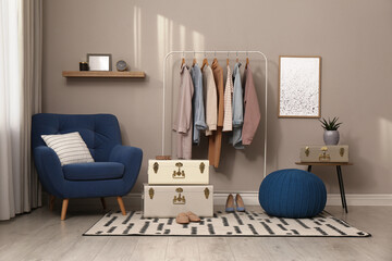 Stylish room interior with comfortable armchair, clothes and storage trunks