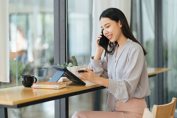 Young woman talking on mobile phone while working with tablet at desk. Home office