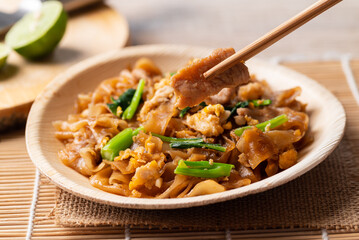 Thai food (Pad See Ew), Stir fried rice noodles with soy sauce, egg, kale and pork eating by use chopsticks