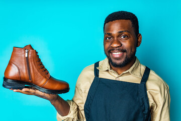latin hispanic man in black apron showing brown leather shoes in blue studio background