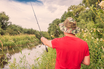 Fisherman in a panama hat and a red t-shirt casts a spinning rod.