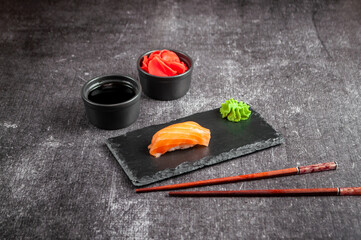 Japanese sushi on a black board with soy sauce, ginger and wasabi on a gray dark background