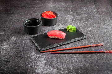 Japanese sushi on a black board with soy sauce, ginger and wasabi on a gray dark background