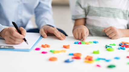 Private child lessons. Little boy counting colorful numbers, studying with professional woman...