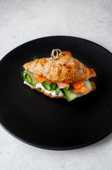 Croissant with vegetables and salmon on a dark plate on a light gray background
