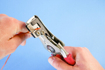 An electrician removes insulation from a copper wire. Working with the tool. Stripper work close-up. Device for removing insulation from electric cables.