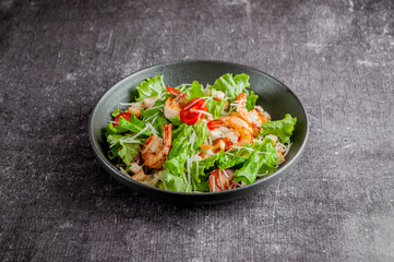 Salad with vegetables and shrimp in a dark dish on a gray background