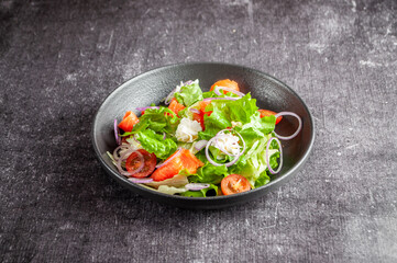 Salad with vegetables and salmon in a dark dish on a gray background