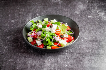 Vegetable salad with feta cheese in a dark dish on a gray background