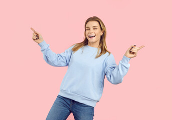 Cheerful teenage girl laughing, having fun and dancing, isolated on pastel pink background. Smiling girl in casual light blue hoodie and jeans celebrating her success. Banner. Copy space.